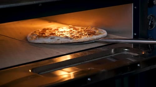 Putting pepperoni pizza into the oven in a restaurant kitchen.
