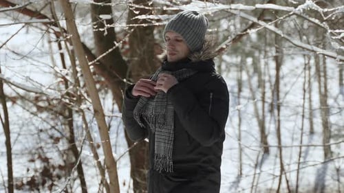 Serious European Man Adjusts Scarf Around His Neck in Winter Sunny Forest