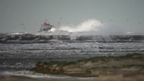 Wild coastal storm waves batter IJmuiden lighthouse and pier with ship in back