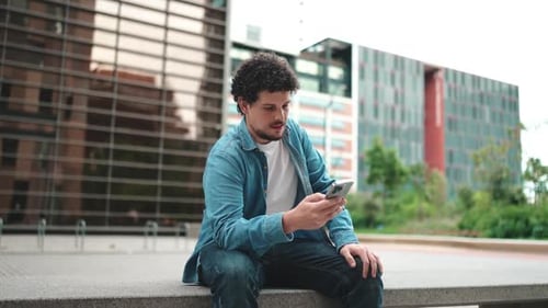 man sitting and using mobile phone in the street modern buildings background