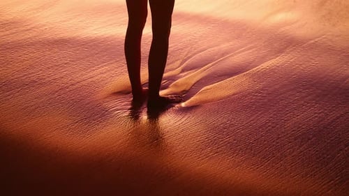 Woman stands on the beach on Mahé Island in Seychelles during a beautiful warm sunset. She dips her