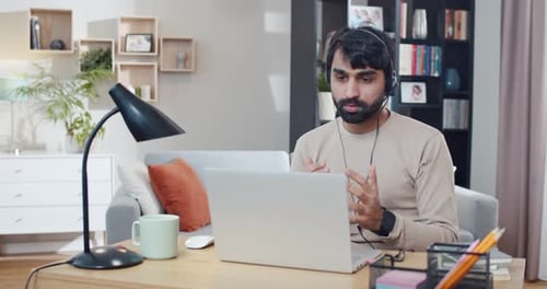 Arabian Young Man in Headset Working at Computer and Talking While Videochatting at Home Call Center