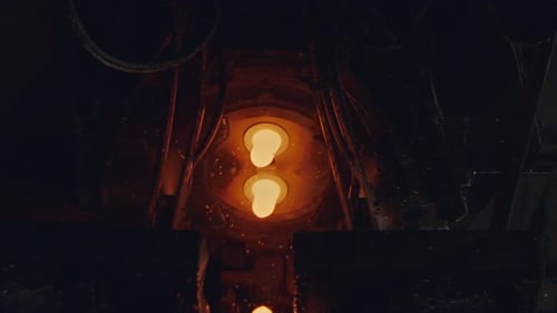 Slow motion of Molten glass pouring out of a Glass melting furnace in a bottle production facility.