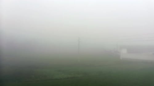 Electricity pole appearing slowly on a field in the countryside full of fog.