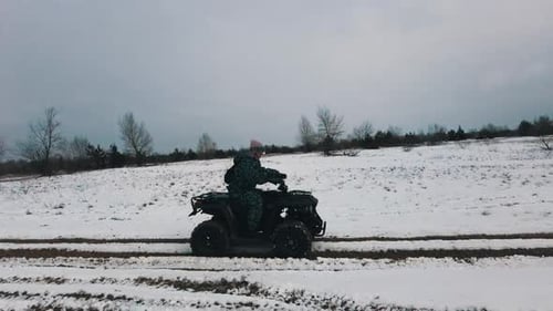 Woman Riding on an ATV Through the Snowy Landscape Side View