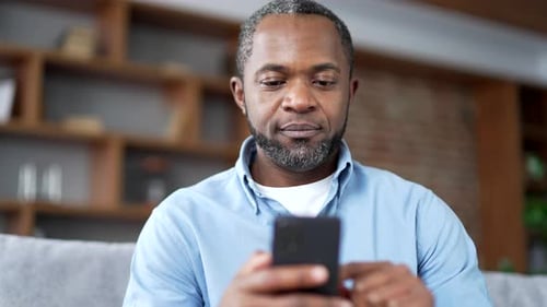Man Looks at his Mobile Phone at Home