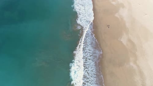 Aerial view of the waves of the blue sea breaking on the sand of a beautiful long white sand beach a