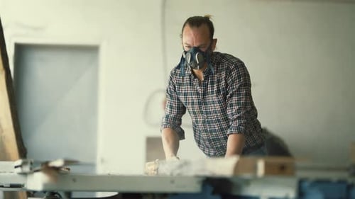 Carpenter with Respirator Mask Sawing Wood Plank