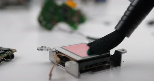 Closeup of a brush brushing disassembled camera sensor on the desk in workshop. Broken camera for se