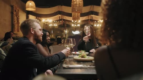 Des amis multiethniques fêtent leur anniversaire au restaurant, une femme porte un toast et des gens tintent des verres
