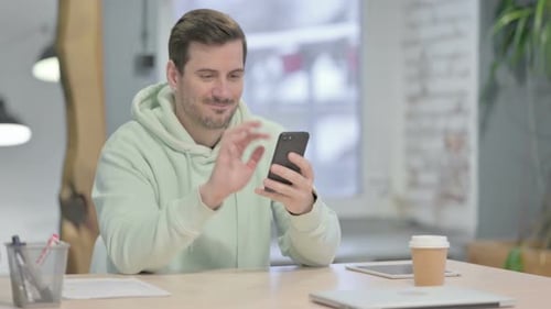 Man Reacts to Phone at Desk Indoors