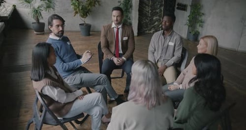 Therapist Talking to Multiethnic Group of People Sitting in Circle in Rehab Center While Men and