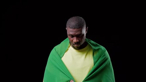 Holding Brazil flag, adult man pulling flag around shoulders, showing pride under studio lights