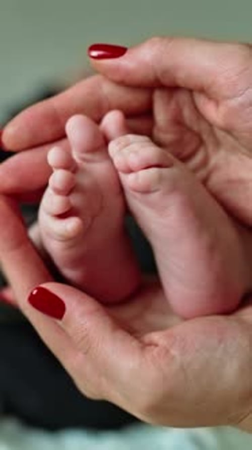 Careful loving mommy's hands hold tiny baby feet. Little child moves his cute toes. Close up.