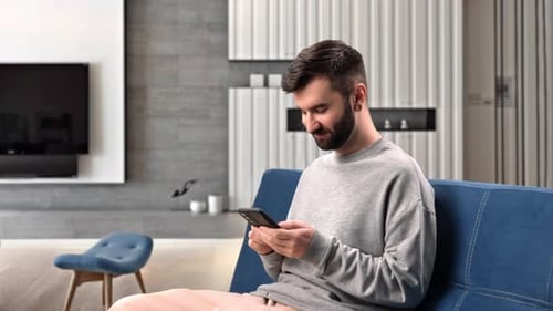 Bearded Man Using Smartphone on Couch at Home