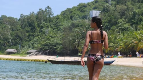 Back View of Young Woman in Bikini Walking in the Clear Water at the Beach