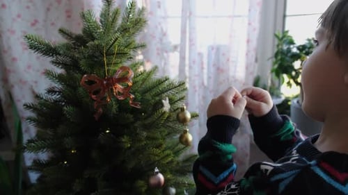 Child Decorates Christmas Tree with Shiny Ornaments