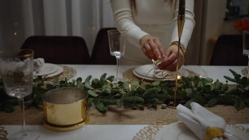 Woman Arranges Holiday Table with Garland and String Lights