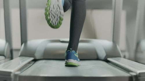 Nahaufnahme athletischer Füße, die auf einem Laufgerät im Fitnessstudio laufen. Ansicht von hinten