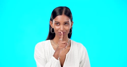 Secret, face and happy woman with finger on lips in studio, blue background or privacy sign