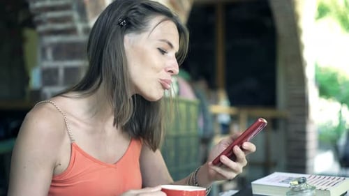 Young Woman Texting on Smartphone and Drinking Coffee in Cafe 30s