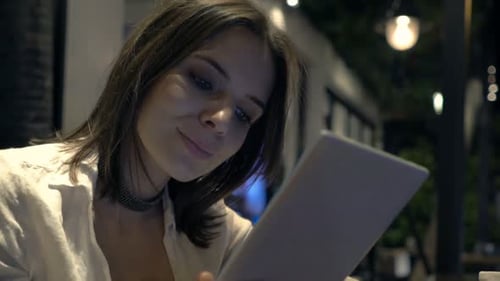 Young woman browsing on tablet computer relaxing in cafe at night