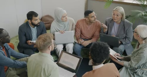 Diverse Group of Colleagues Discussing Business Project Sitting in Circle and Talking in Coworking