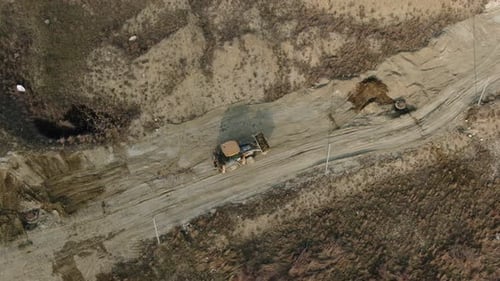 Aerial View of a Yellow Tractor with a Bucket Full of Soil Which is Excavating on a Dirt Road