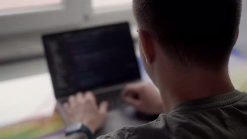 Vue arrière au-dessus de l'épaule d'un homme qui travaille sur un programmeur d'ordinateur portable