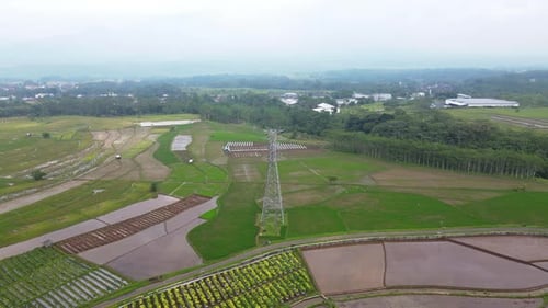 Drone shot of electricity tower on the middle of plantation in cloudy sky