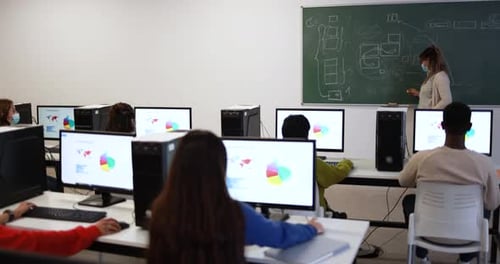 Multiracial students and teacher wearing face masks inside computer classroom at college