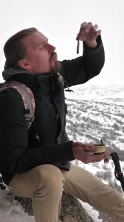 Man Eating Food While Sitting on Snowy Mountain