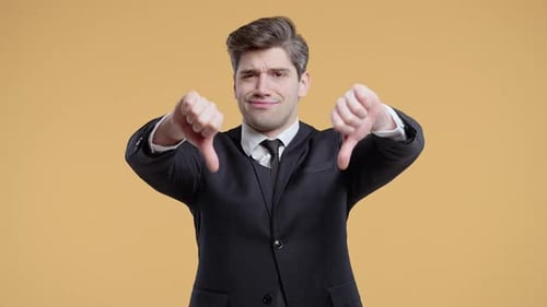 Businessman in Suit Giving Thumbs Down Dislike with Disapproving Look on Beige