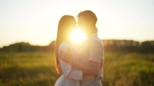 Loving Young Man and Woman Walking Toward Each Other Hugging and Kissing in Field on Background of