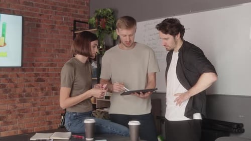 Three Colleagues Discuss a Project Using a Tablet in Their Office