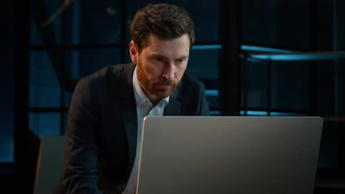 Focused Man Working on Laptop in Dimly Lit Office