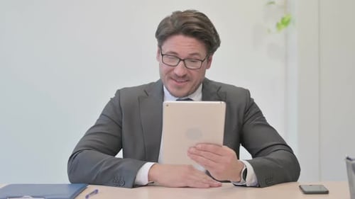 Video Call on Tablet by Middle Aged Businessman in Office