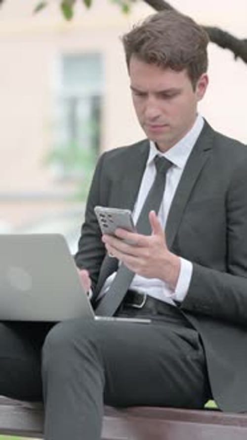 Man Sits on Bench Using Laptop and Phone