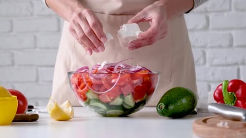 Femme ajoutant du fromage feta à un bol de salade grecque