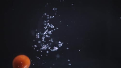 Slow motion shot of cherry tomatoes falling in water. Floating fruit dropped in water on black backg