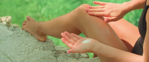 Applying sunscreen outdoors. A person smears cream on her leg, importance of skin protection, sun ca