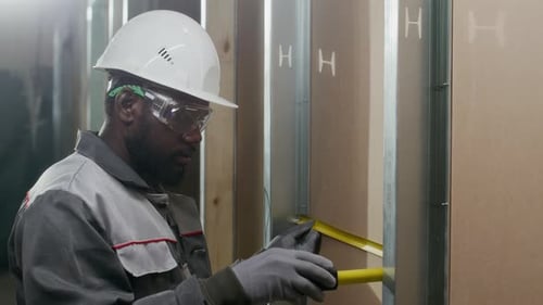 Young Builder Using Measuring Tape at Office Space under Construction