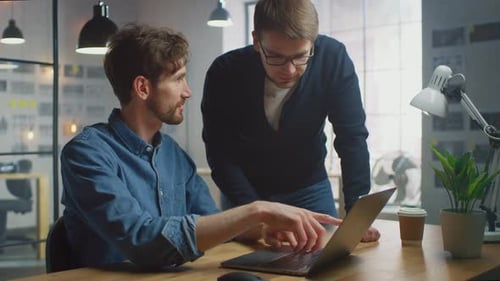 Two Handsome Creative Colleagues Talk about Worksand Discuss it on a Laptop Computer in Their Sunny