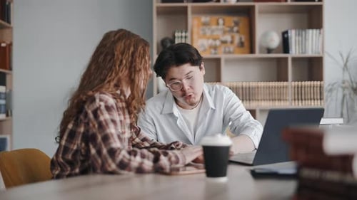 Two students collaborating on a project in a library using a laptop