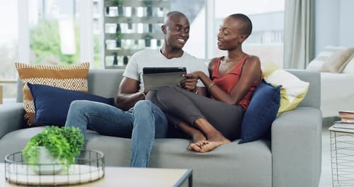 Couple Smiles Looking at Tablet on Sofa