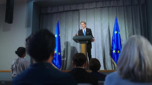Man Giving Speech with Audience Raising Hands