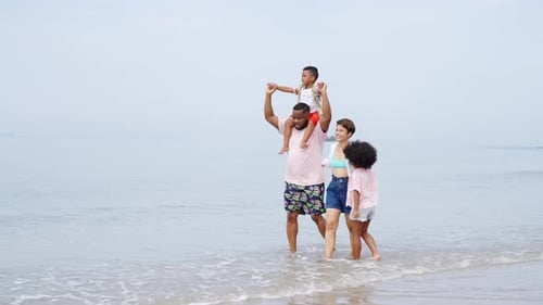 4K African family walking together on the beach at summer sunset.