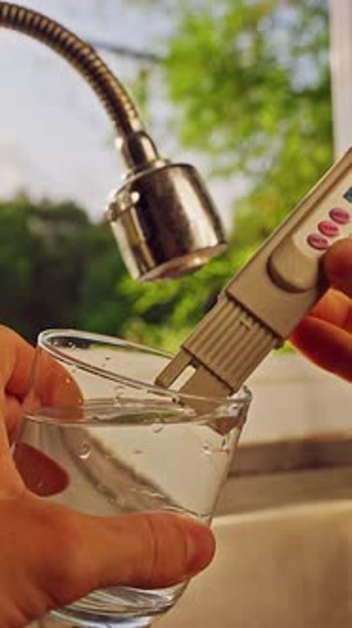 Vue à la première personne des mains mesurant l'eau potable avec un testeur de qualité numérique en verre transparent à proximité