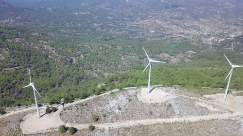 Aerial footage of Wind turbines spinning, in a mountain forest surrounding