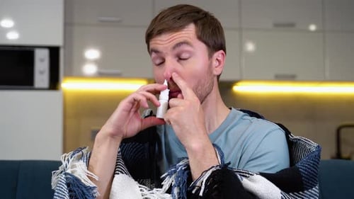Man Administers Nasal Spray While Seated on Couch